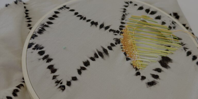 Detail of a piece of fabric being mended with yellow and orange thread